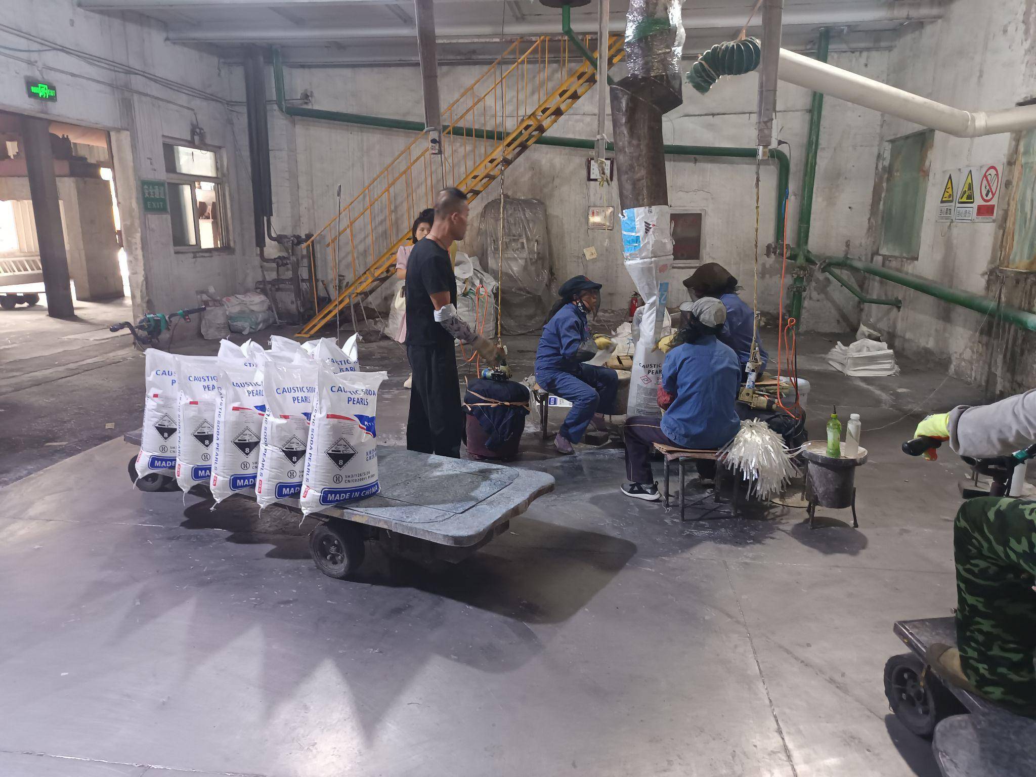 Workers filling and sealing 25 kg bags of caustic soda pearls inside a chemical production facility in China.